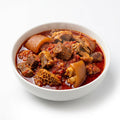 A white ceramic bowl filled with a rich, reddish-brown stew containing beef chunks, nettle, and a large piece of trotter, set against a clean white background.