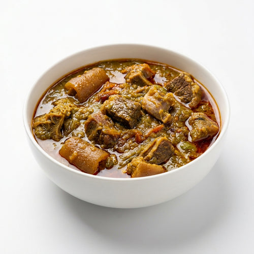 A white ceramic bowl filled with a rich, chunky stew containing green vegetables, brown root vegetables, and meat in a reddish-brown broth, set against a clean white background.