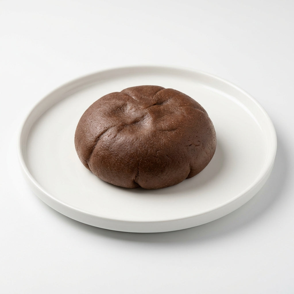 A single dark brown baked bun or bread roll centered on a round white plate against a clean white background.