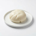 A steamed bun or baozi dumpling on a round white ceramic plate, set against a clean white background.